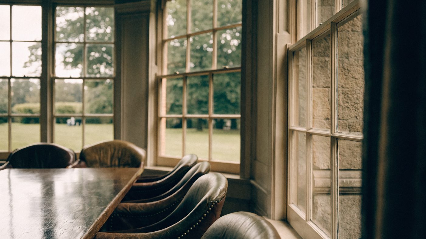 A private committee room in an English golf club, long polished table and leather chairs beside tall windows looking onto a green