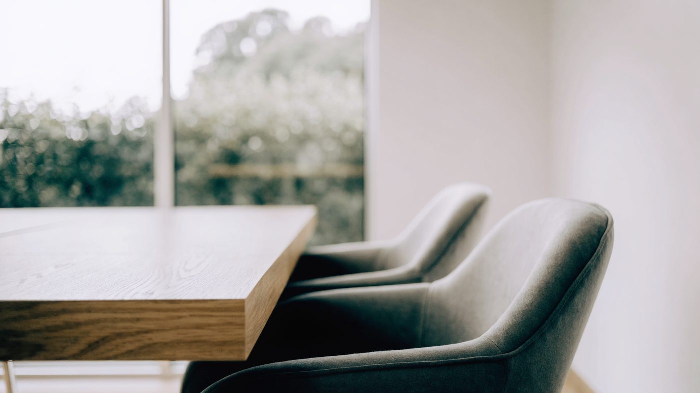 A clean, contemporary meeting room in a modern business park, pale oak table and soft grey chairs beside a full-height window
